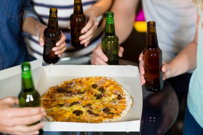 Mid section of friends having bottle of beer and pizza in party at bar